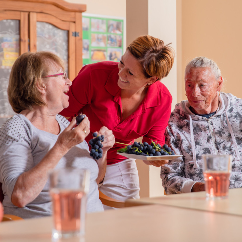 Betreuerin unterhält sich mit zwei Bewohnerinnen bei einer gemeinsamen Obst-Jause.